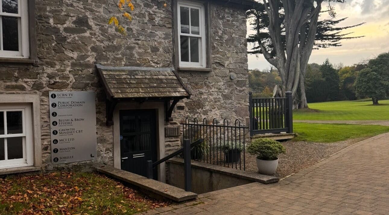 Charming stone building at MyRevibe, Douglas, IM surrounded by lush greenery and serene pathways.