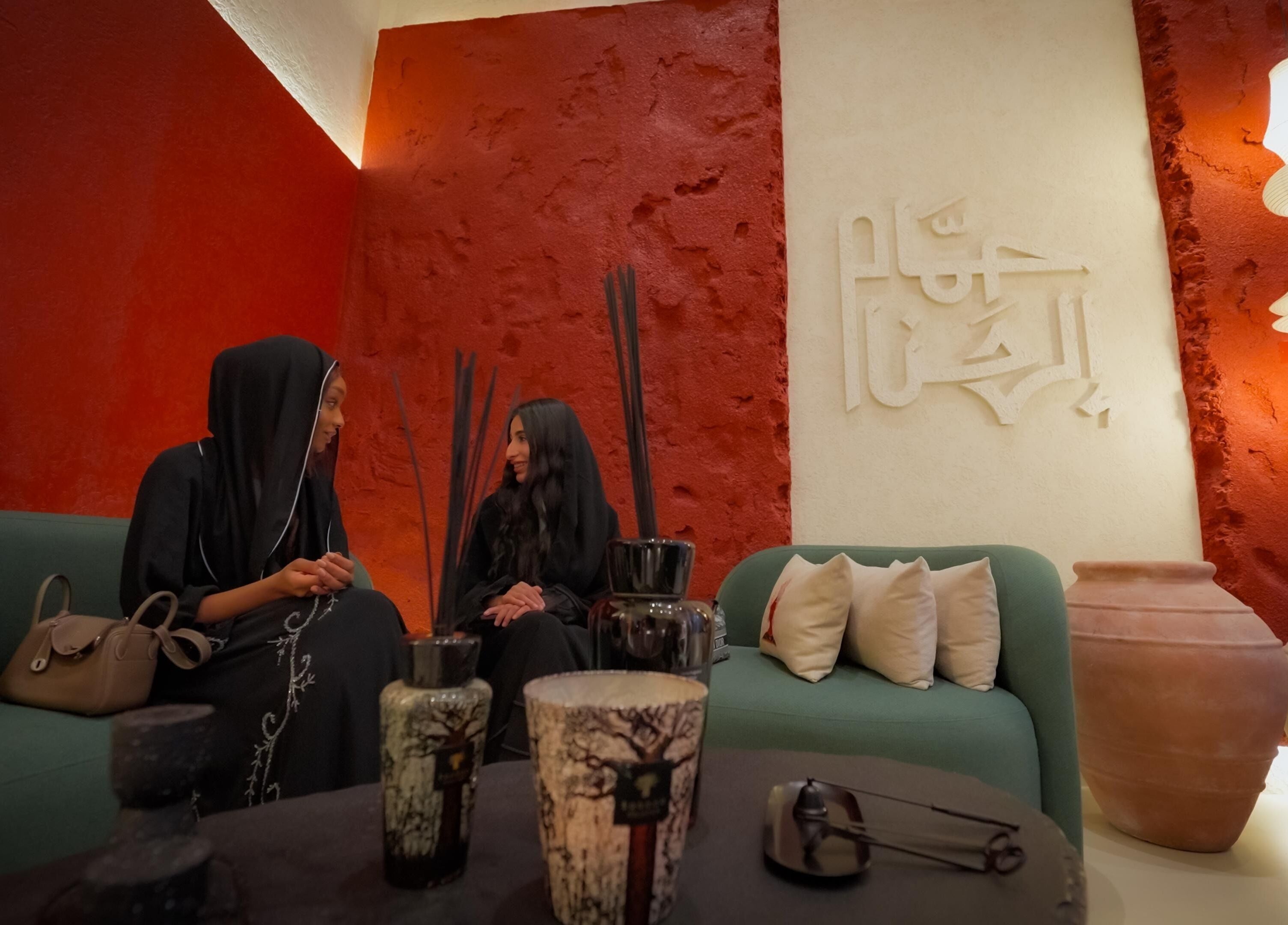 امرأتان تتحدثان في ردهة حمام الهنا، الرياض، الرياض، SA بجانب جدار أحمر وديكور أنيق.