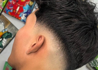 Corte de pelo estilo fade en Mcky Barber Studio, Cancún, Quintana Roo, MX, con obras de arte coloridas al fondo.