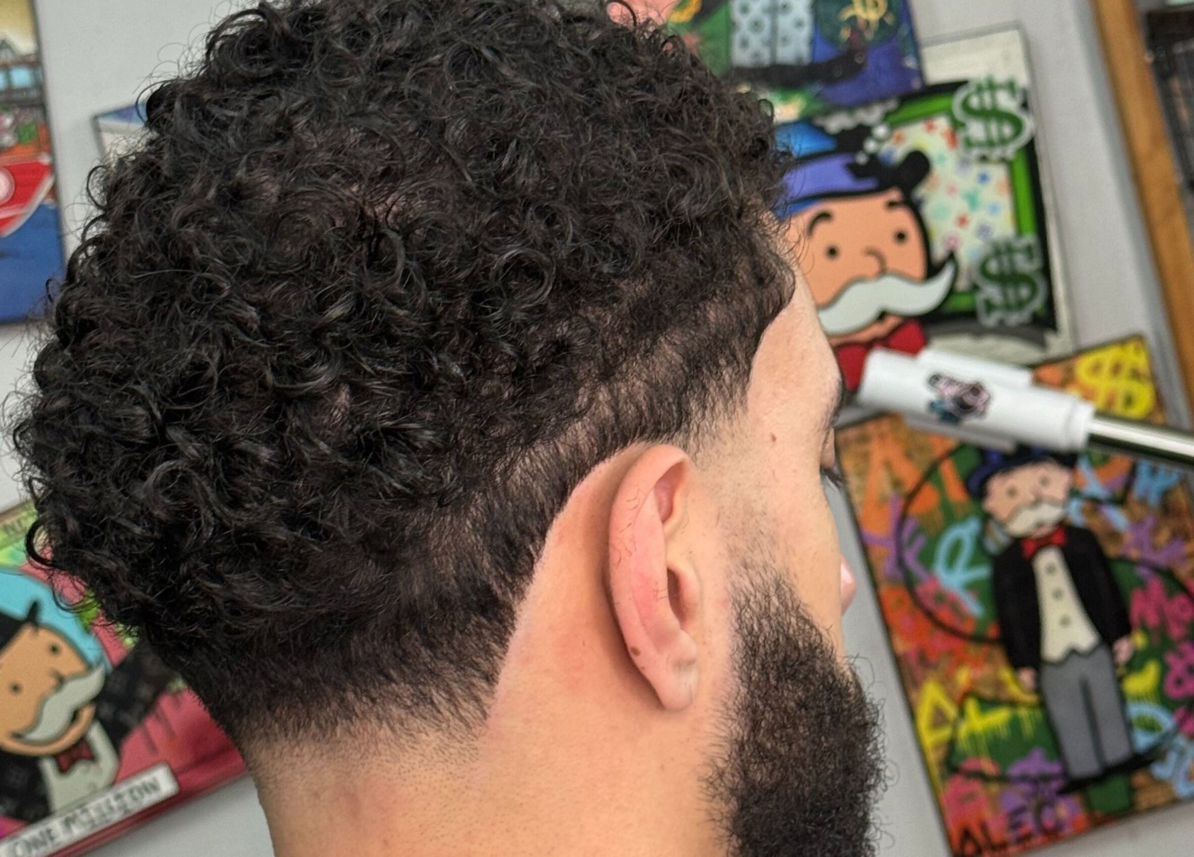Corte de cabello rizado en Mcky Barber Studio, Cancún, Quintana Roo, MX, con arte urbano de fondo.