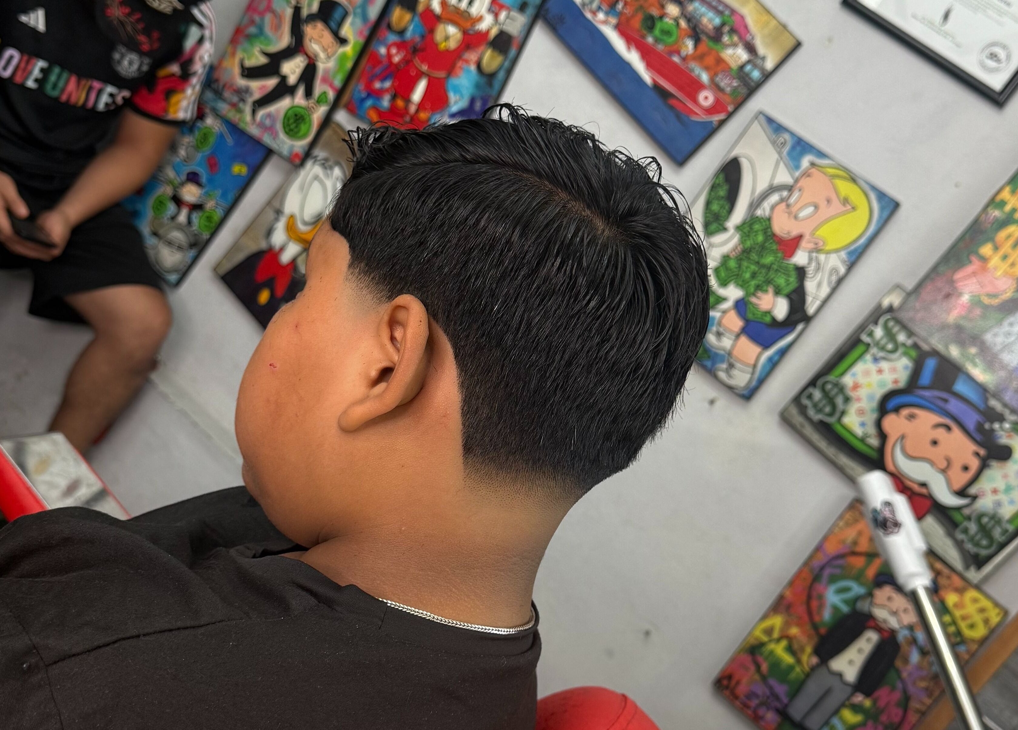 Corte moderno en Mcky Barber Studio en Cancún, Quintana Roo, MX, con arte colorido en las paredes.