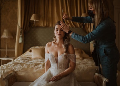 Bridal hairstyling at Emma Combe Hair in North Berwick, Scotland, GB. Elegant bride on bed with stylist.
