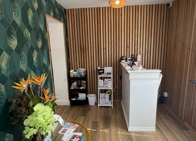 Reception area of Blooms Beauty Room, Burgess Hill, England with tropical plant decor and wooden accents.