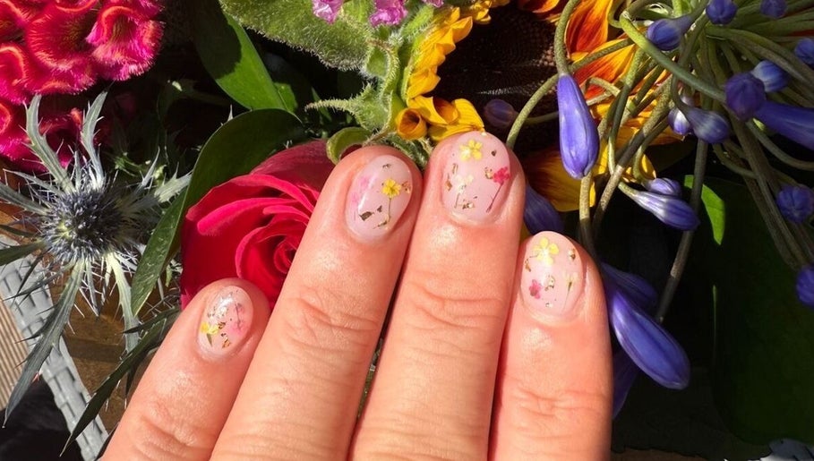Floral nail art at Alex at Beauty Secrets in Douglas, IM displayed against vibrant flower backdrop.