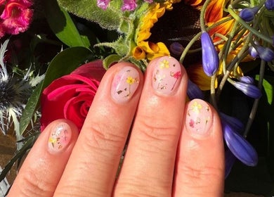 Floral nail art at Alex at Beauty Secrets in Douglas, IM displayed against vibrant flower backdrop.