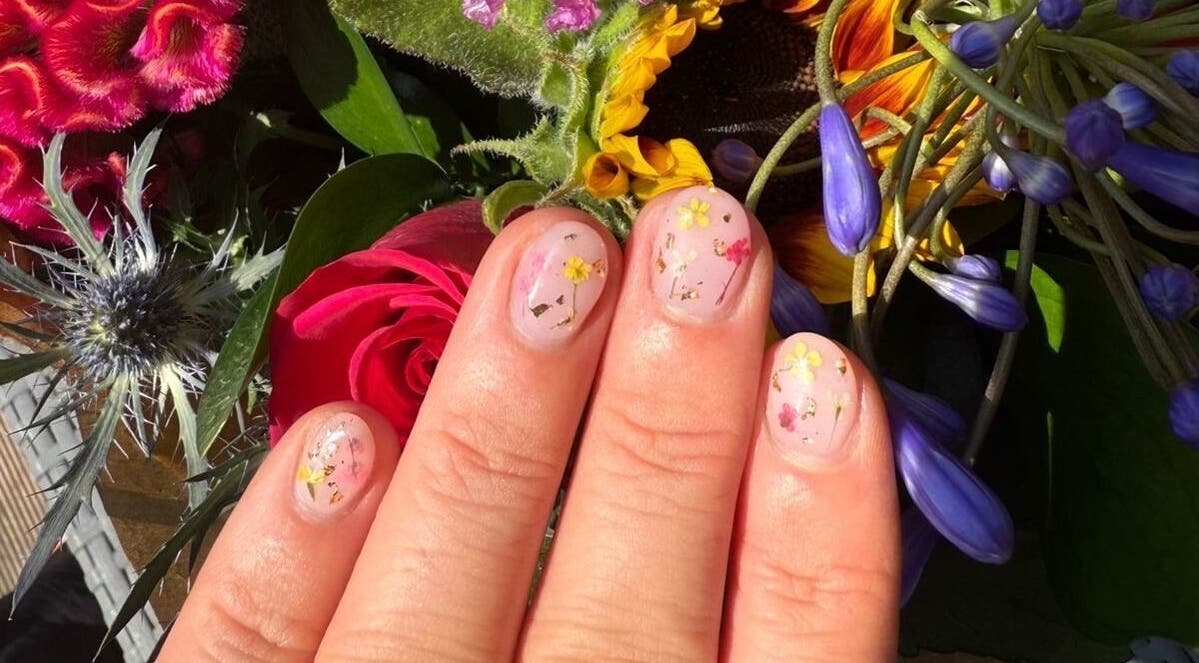 Floral nail art at Alex at Beauty Secrets in Douglas, IM displayed against vibrant flower backdrop.