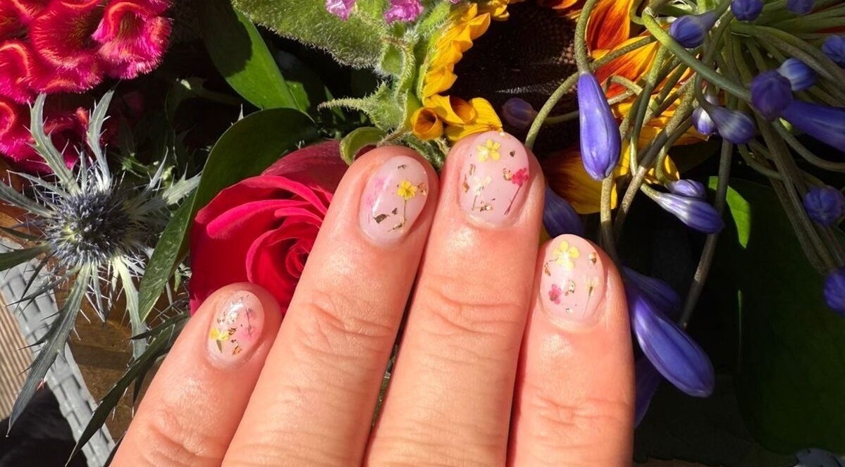 Floral nail art at Alex at Beauty Secrets in Douglas, IM displayed against vibrant flower backdrop.
