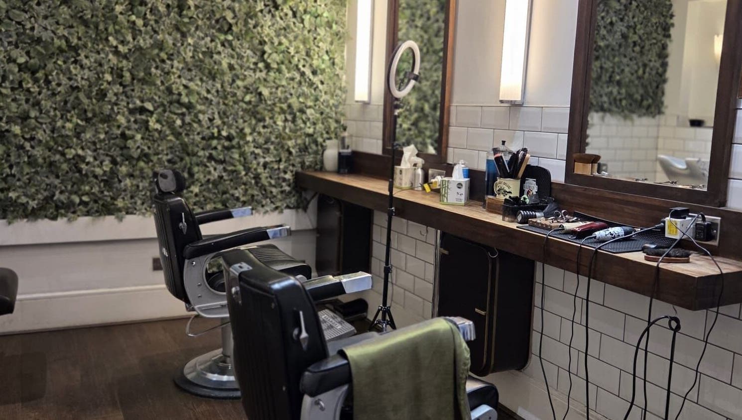 Chic barber chairs at The Honest Barber in London, England, GB, with a lush green wall backdrop.