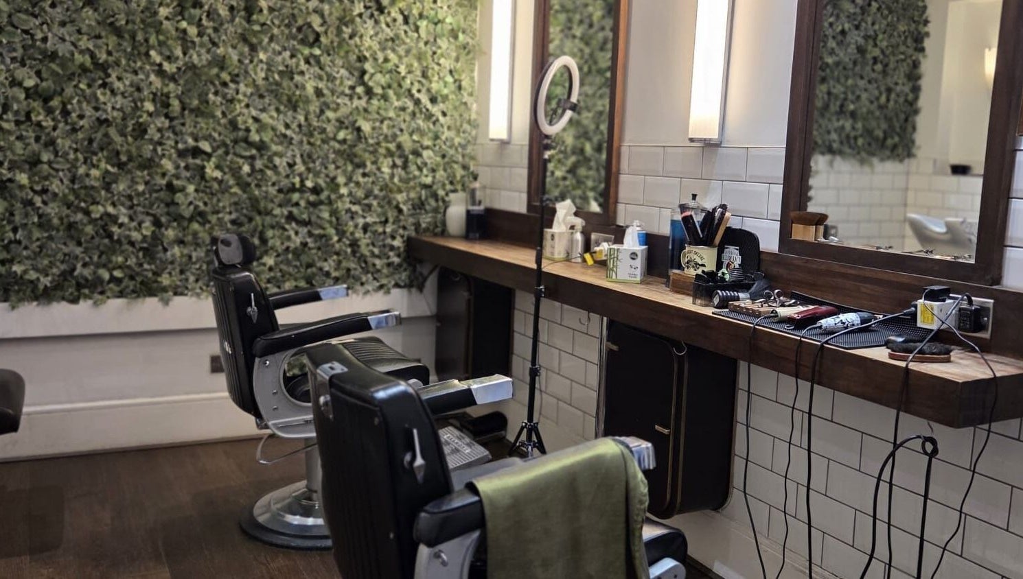 Chic barber chairs at The Honest Barber in London, England, GB, with a lush green wall backdrop.