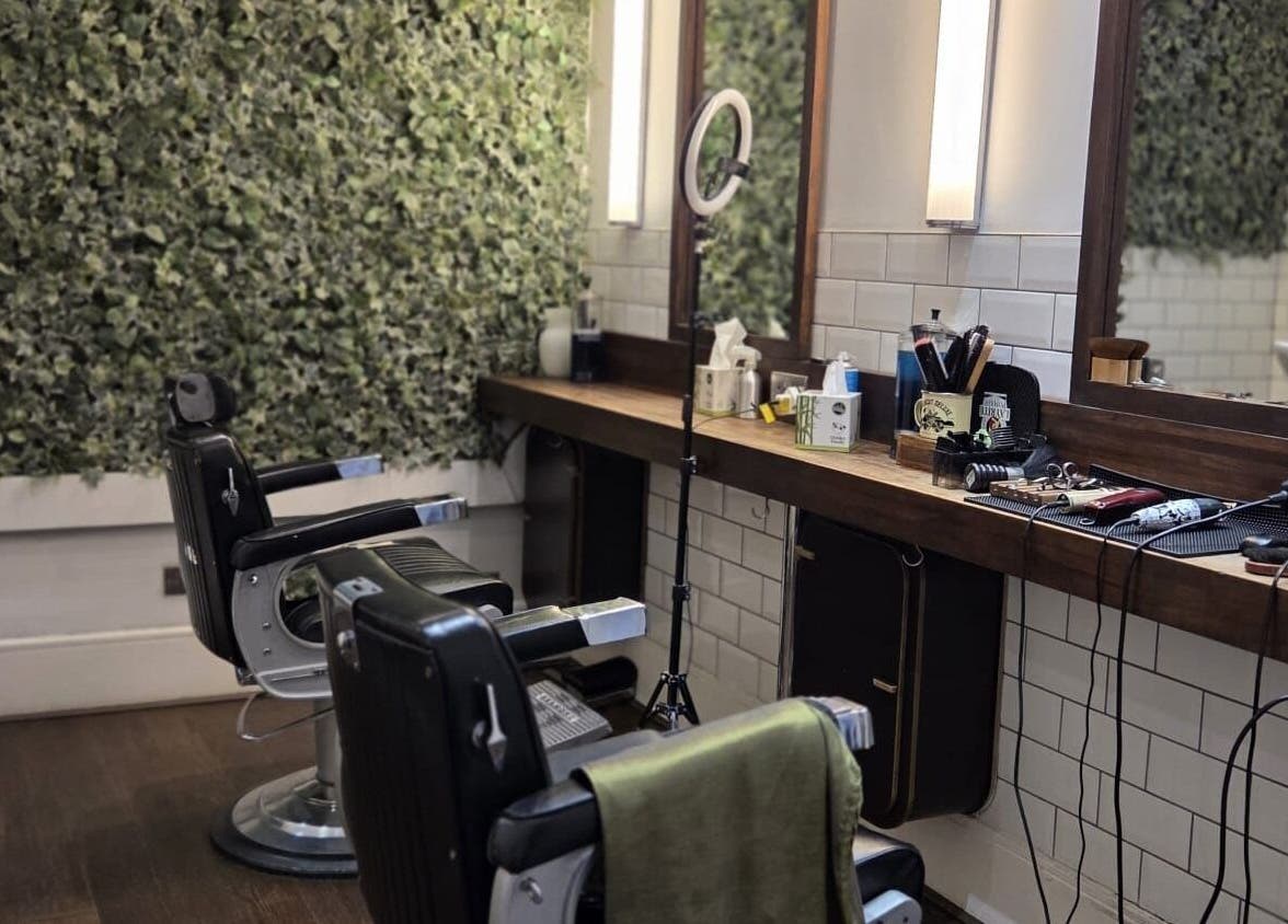 Chic barber chairs at The Honest Barber in London, England, GB, with a lush green wall backdrop.
