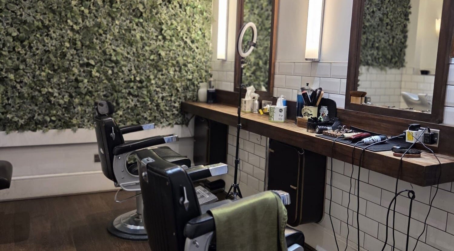Interior of The Honest Barber in London, England, GB, featuring vintage chairs and a green wall.