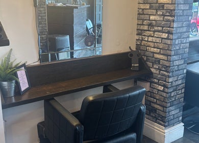 A sleek salon station at The Hair And Beauty Corner, Manchester, England, GB, with mirror and black chair.