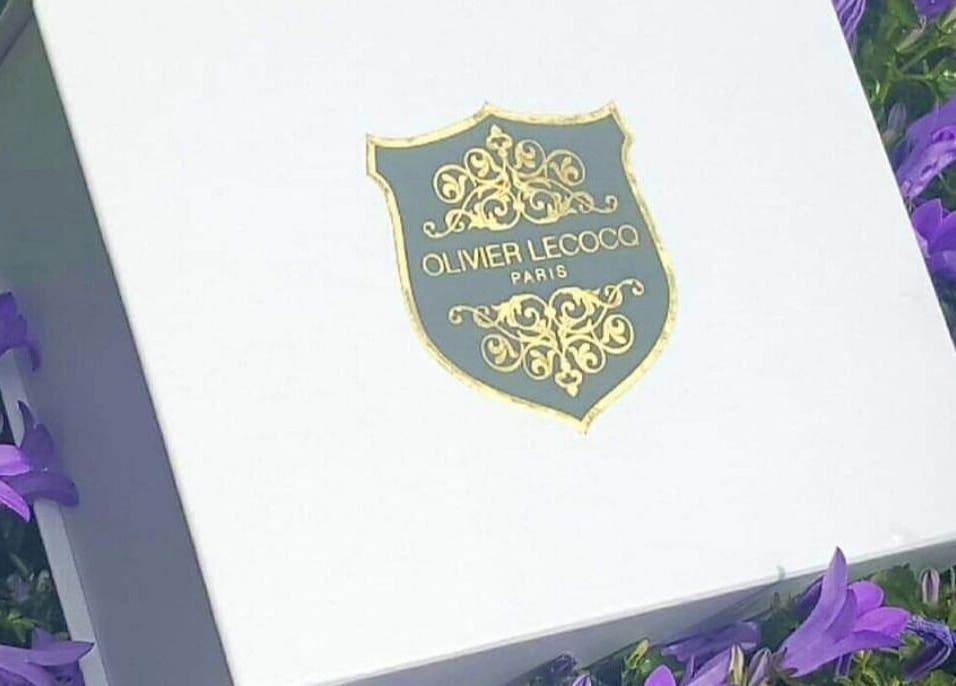 Logo Olivier Lecocq sur boîte élégante entourée de fleurs mauves à L'Atelier du Bien-être par Olivier, Paris, Île-de-France, FR.