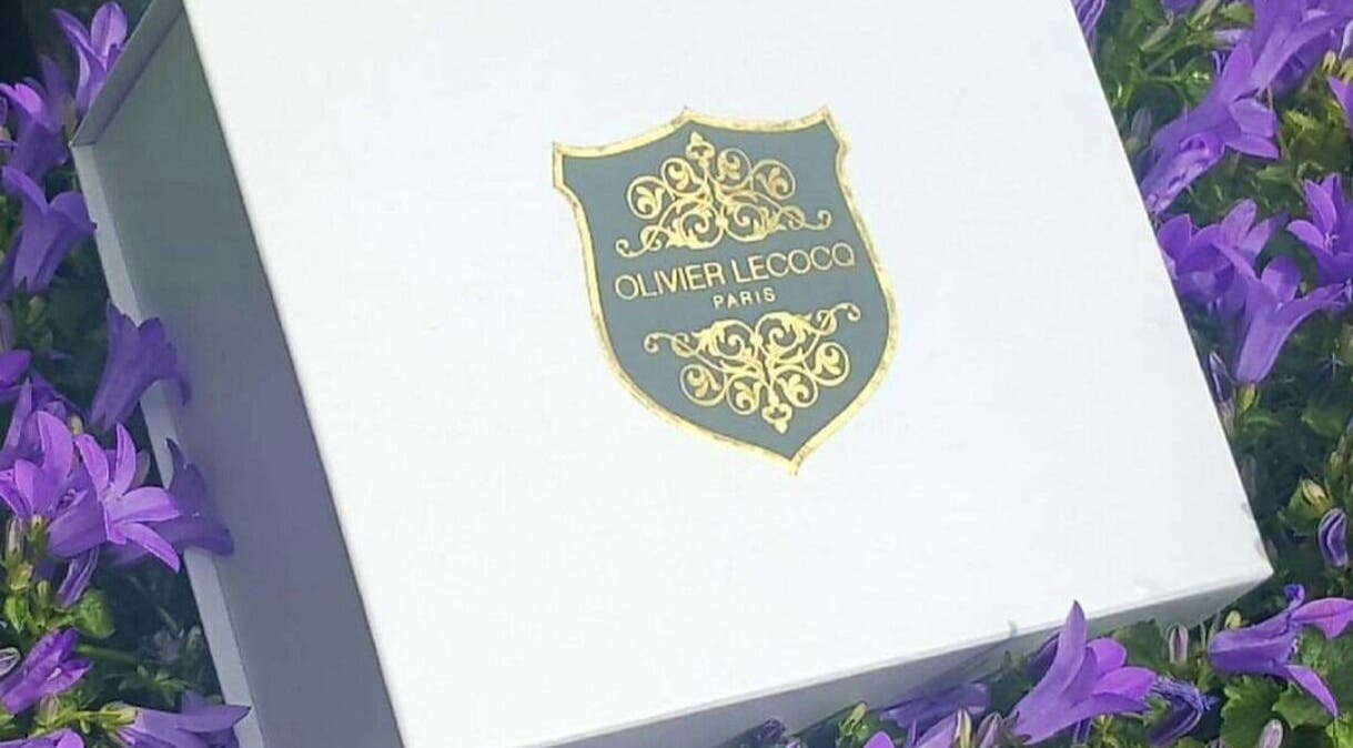 Logo Olivier Lecocq sur boîte élégante entourée de fleurs mauves à L'Atelier du Bien-être par Olivier, Paris, Île-de-France, FR.