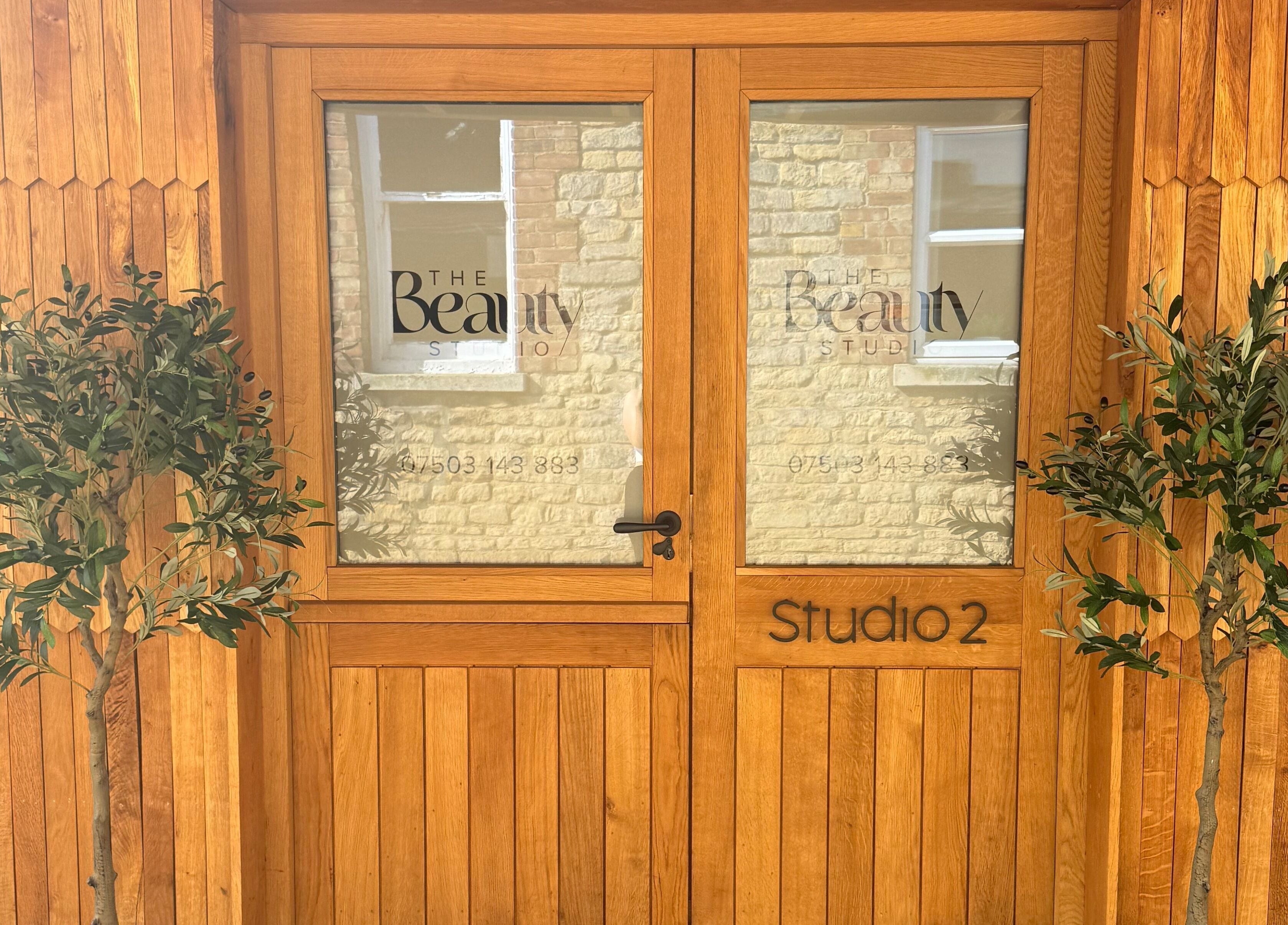 Chic entrance of The Beauty Studio, Peterborough, England, GB, with wooden doors and potted plants.