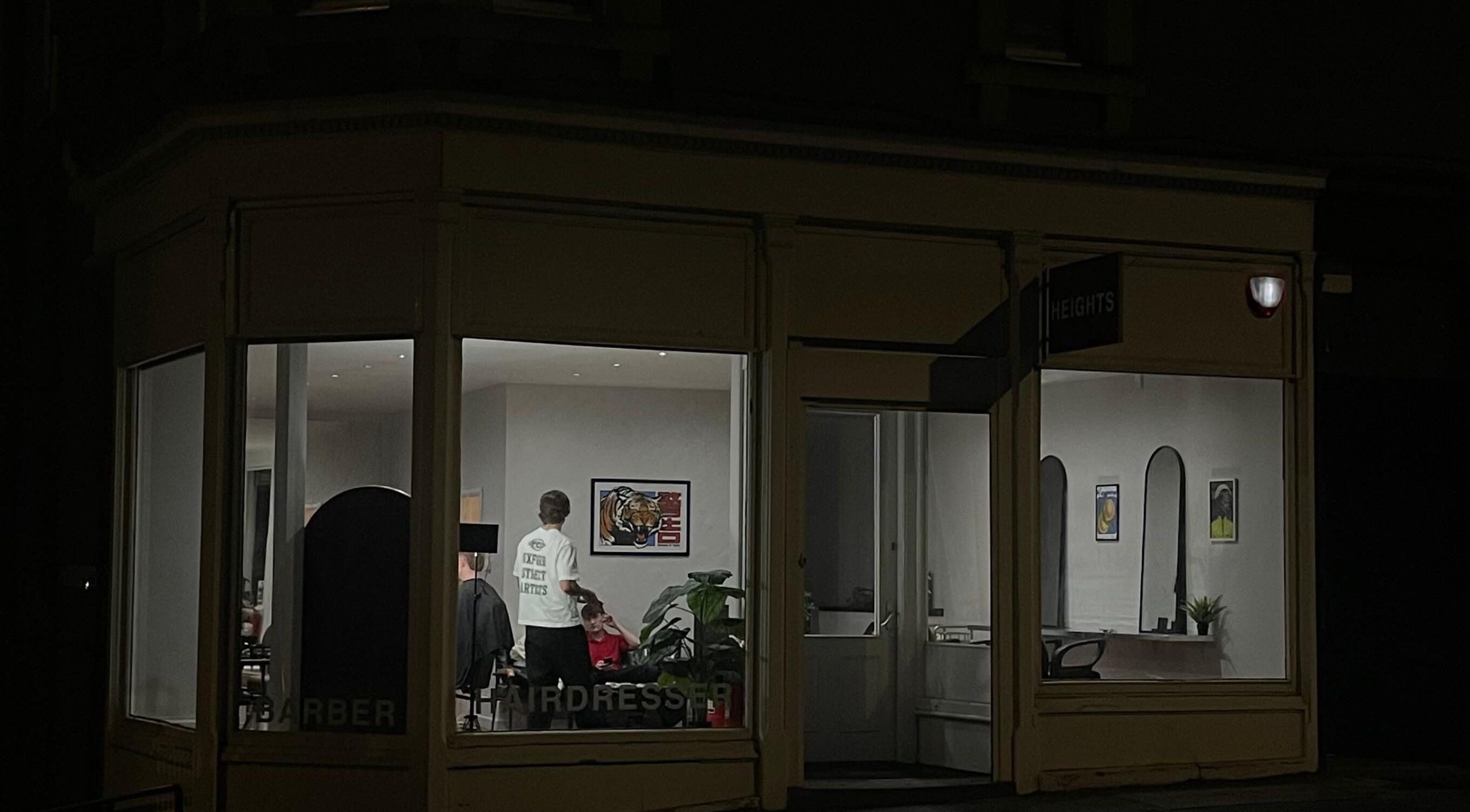 Night view of H E I G H T S salon in Dundee, Scotland, GB with a stylist and client inside.