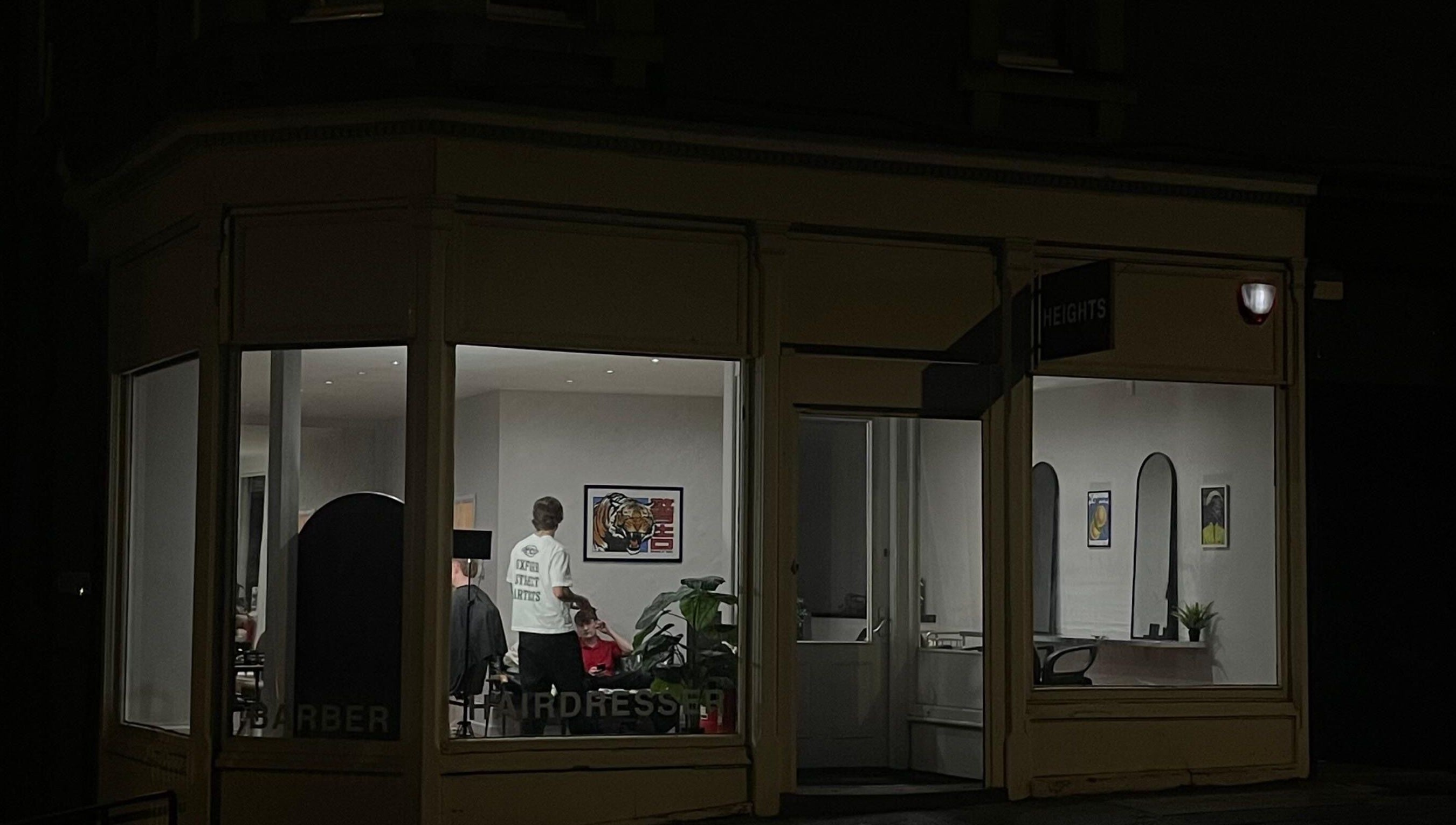 Nighttime view of H E I G H T S barbershop in Dundee, Scotland, GB with interior lighting and stylist present.