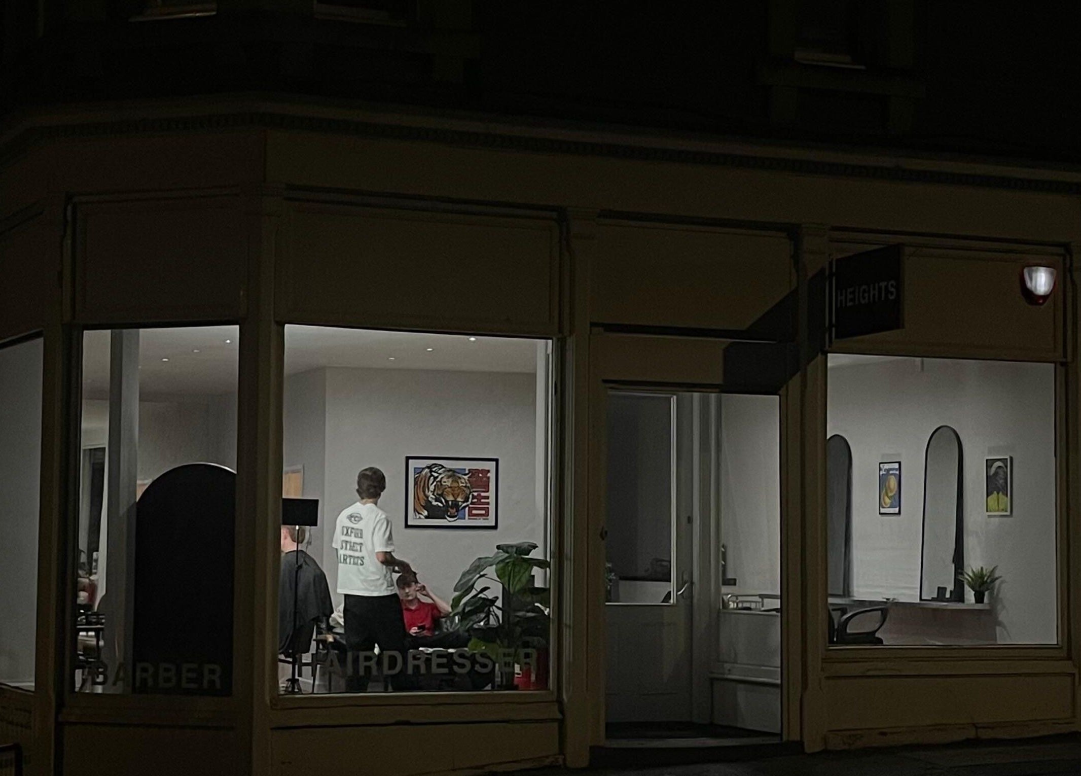 Nighttime view of H E I G H T S barbershop in Dundee, Scotland, GB with interior lighting and stylist present.