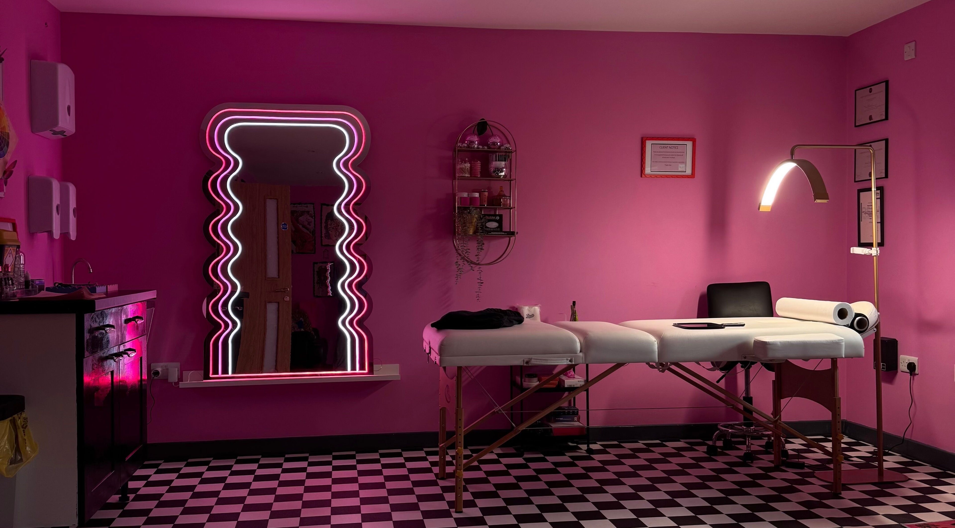 Vibrant treatment room at Naï Beauty Studio, Cardiff, Wales, GB with pink walls, unique neon mirror, and massage bed.