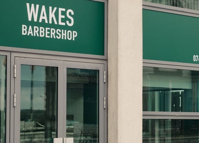 Entrance of Wakes Barbershop in Newquay, England, GB with large glass doors and green signage.