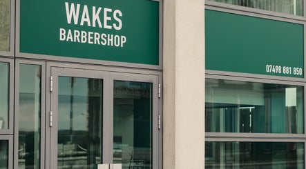 Entrance of Wakes Barbershop in Newquay, England, GB with large glass doors and green signage.