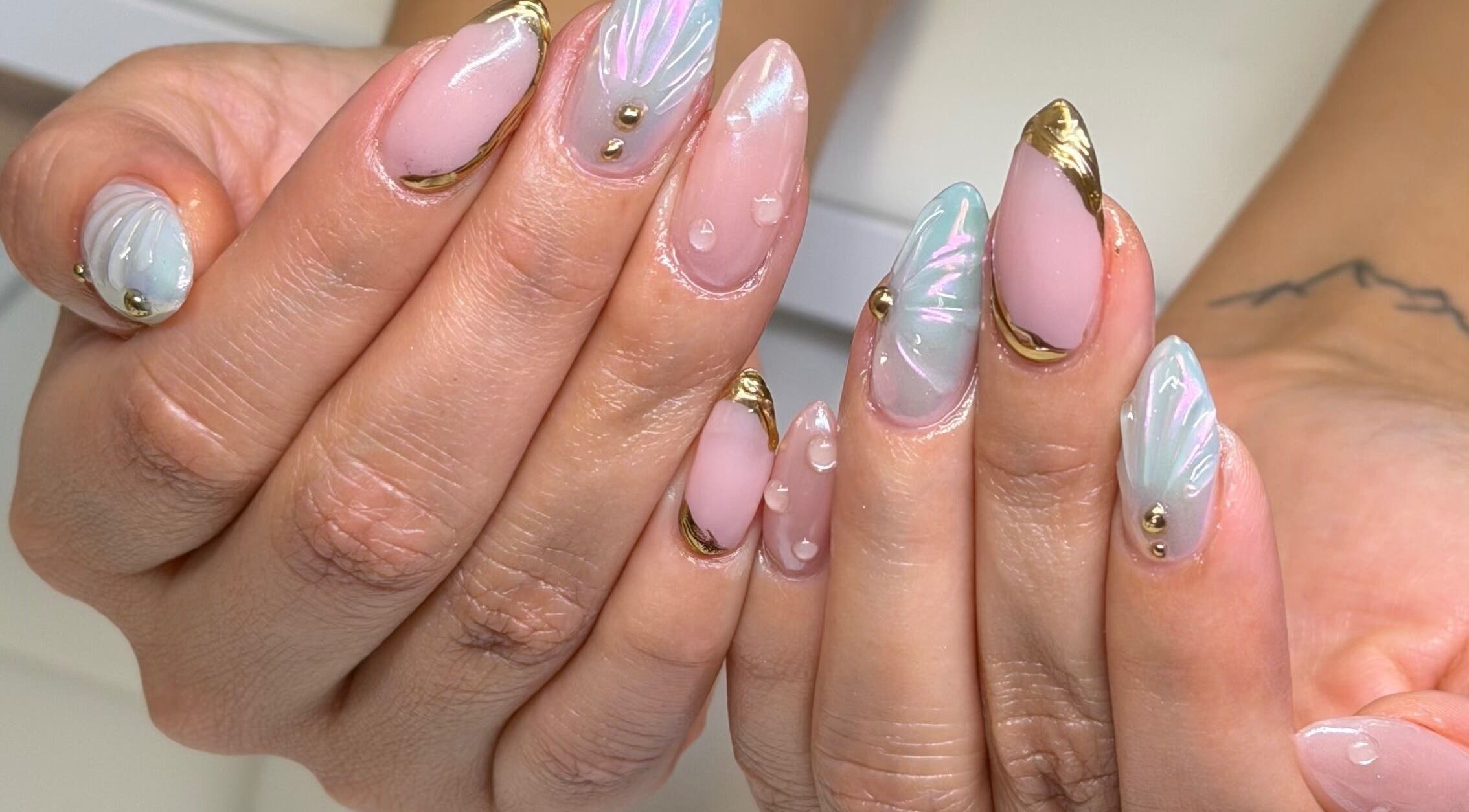 Iridescent nail art design at The Claw Couture, South Jordan, Utah, US, featuring gold tips and pastel hues.