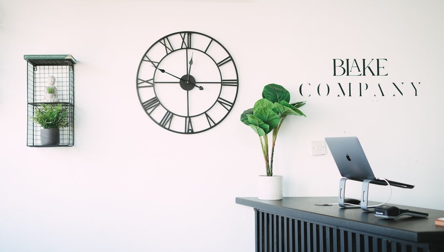Reception area at Blake Company in Kenilworth, England, GB with a clock, plants, and a laptop setup.