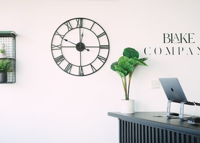 Reception area at Blake Company in Kenilworth, England, GB with a clock, plants, and a laptop setup.