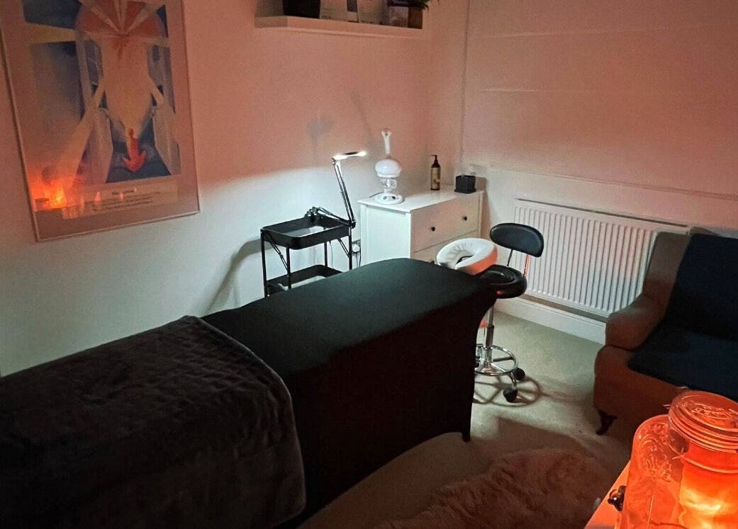 Cozy treatment room at Face Spa in Hastings, England, GB with massage table, plush seating, and soothing lighting.