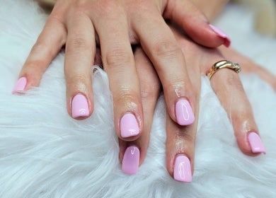 Manicured nails with pink polish from Dark Envy Nails in Swaffham, England, GB on soft, white fur background.