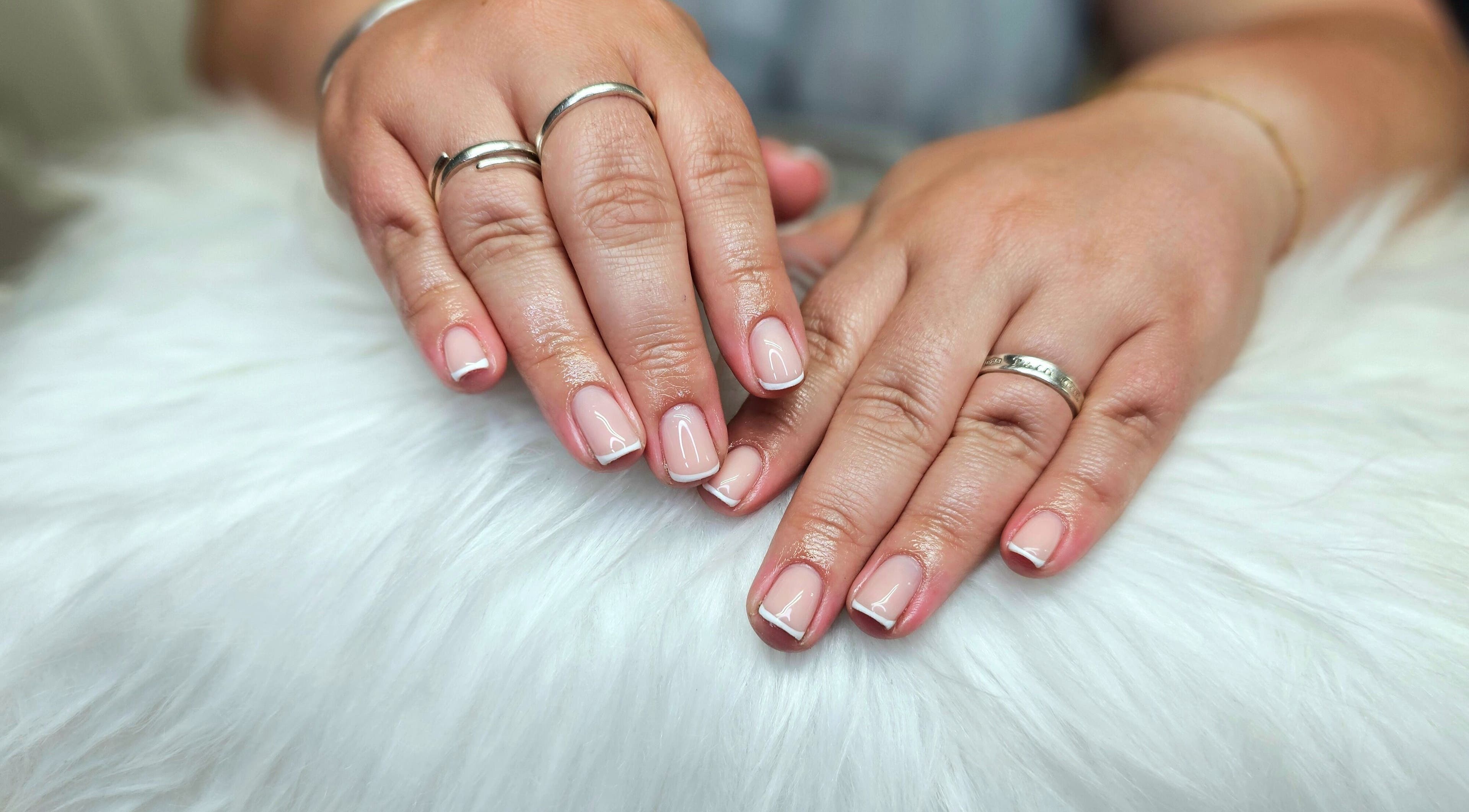 Elegant French manicure at Dark Envy Nails, Swaffham, England, GB. Perfectly polished nails with stylish rings.
