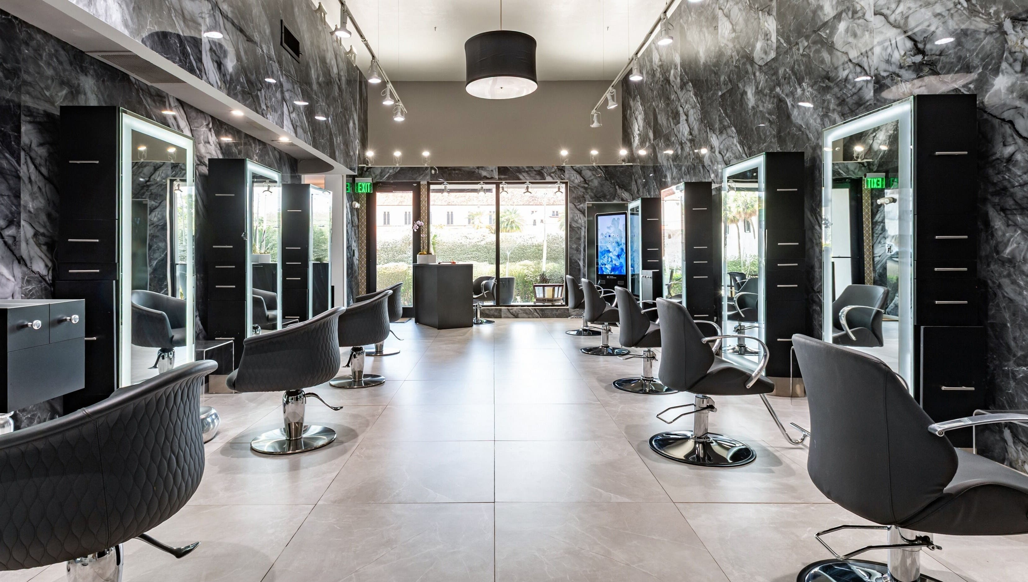 Interior of MG Hair Studios in Coral Gables, Florida, US, featuring modern black styling chairs and illuminated mirrors.