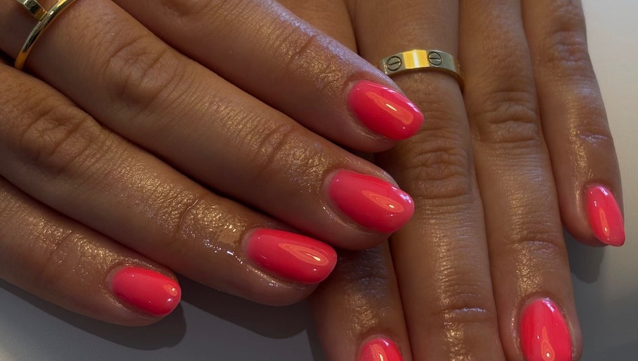 Vibrant pink manicure at AmiRoseBeauté, Barrington, England, GB showcasing elegant nail art and gold rings.