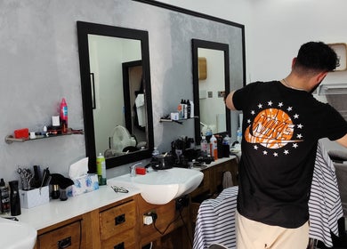 Barber styling hair at Station Barbers Bushill Park, Enfield, England, GB. Modern interior with grooming tools.