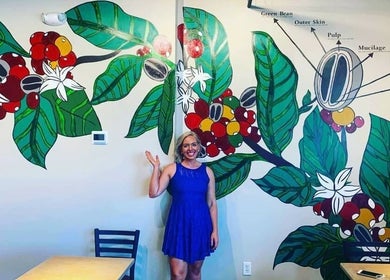 A person in blue dress waves in front of a vibrant floral mural at Barbee Studio, Bowling Green, Kentucky, US.