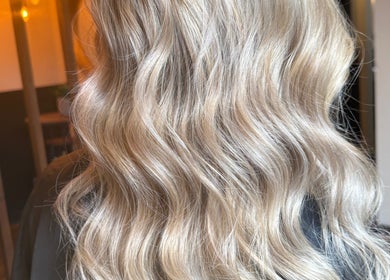 Luxurious, wavy blonde hair styled at Aphrodite in Stirling, Scotland, GB among warm lighting.