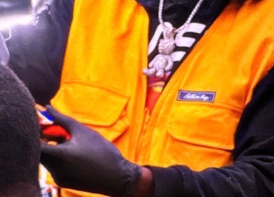 Barber at Faded Barbershop in Detroit, Michigan, US, wearing gloves and orange vest, styling client's hair.
