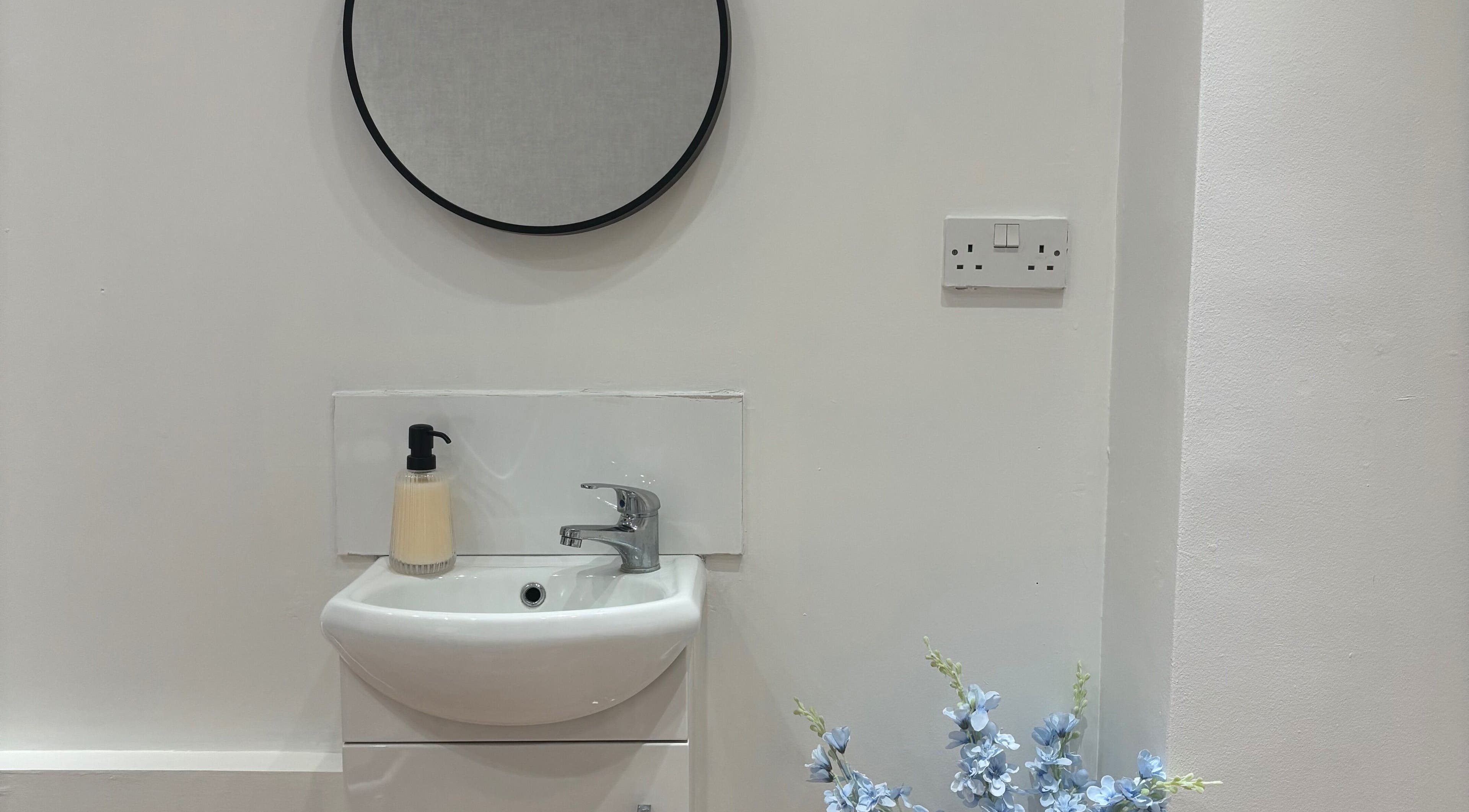 Modern vanity area at By Ells, Redditch, England, GB. Features round mirror and elegant sink.