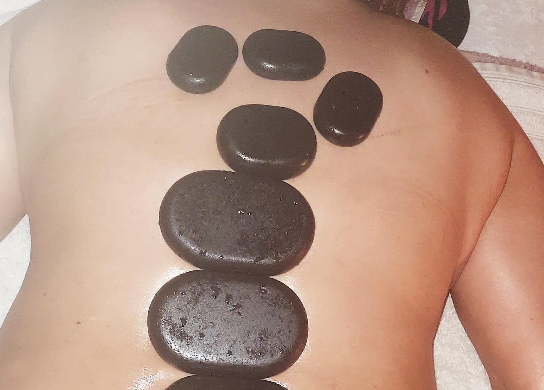 Hotstone massage bij Massagesalon Nostalgia in Alken, BE met warme stenen op de rug.