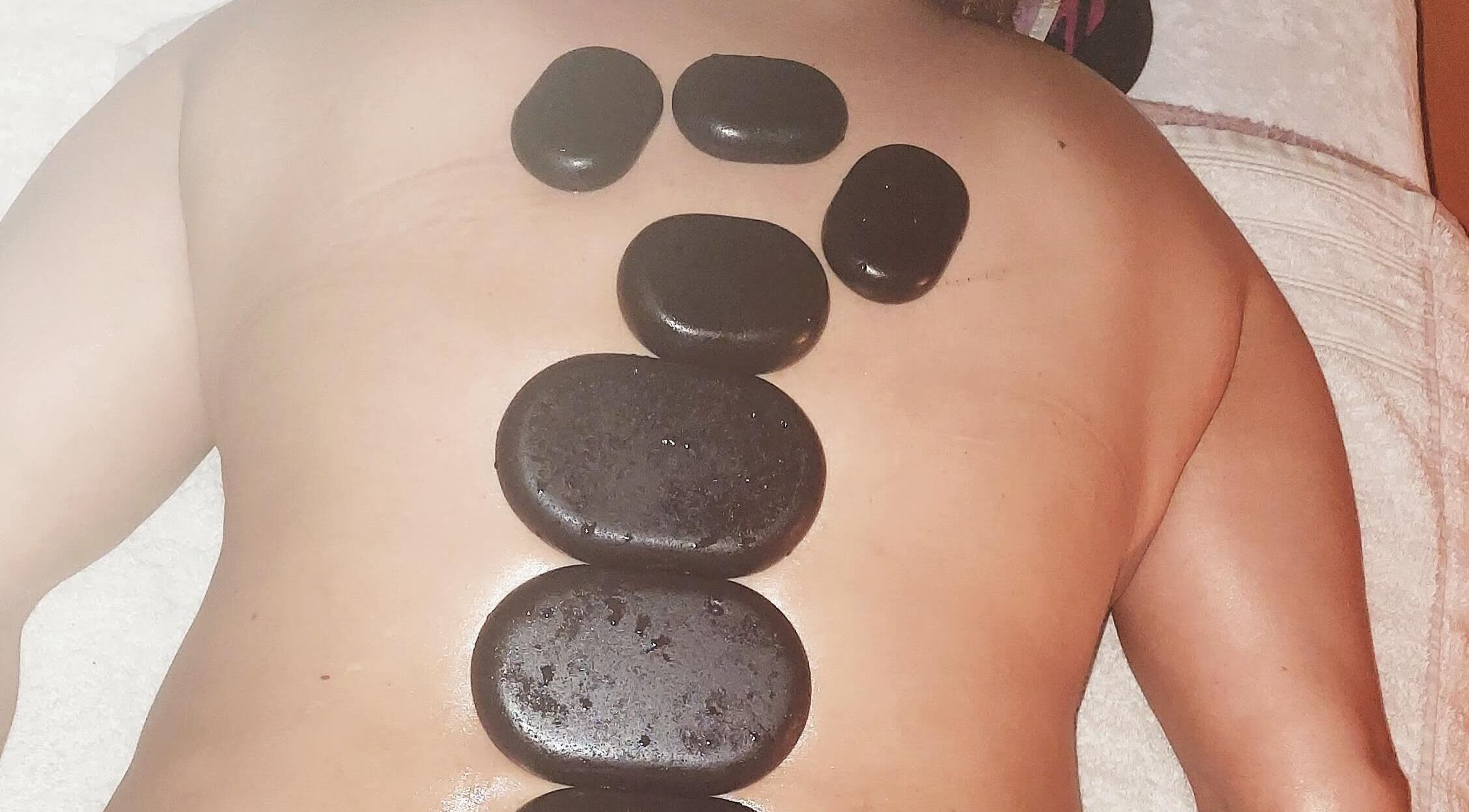 Hotstone massage bij Massagesalon Nostalgia in Alken, BE met warme stenen op de rug.