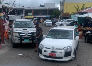 Bustling street near Icons Barbershop, Kingston, St. Andrew Parish, JM with parked cars and local vendors.
