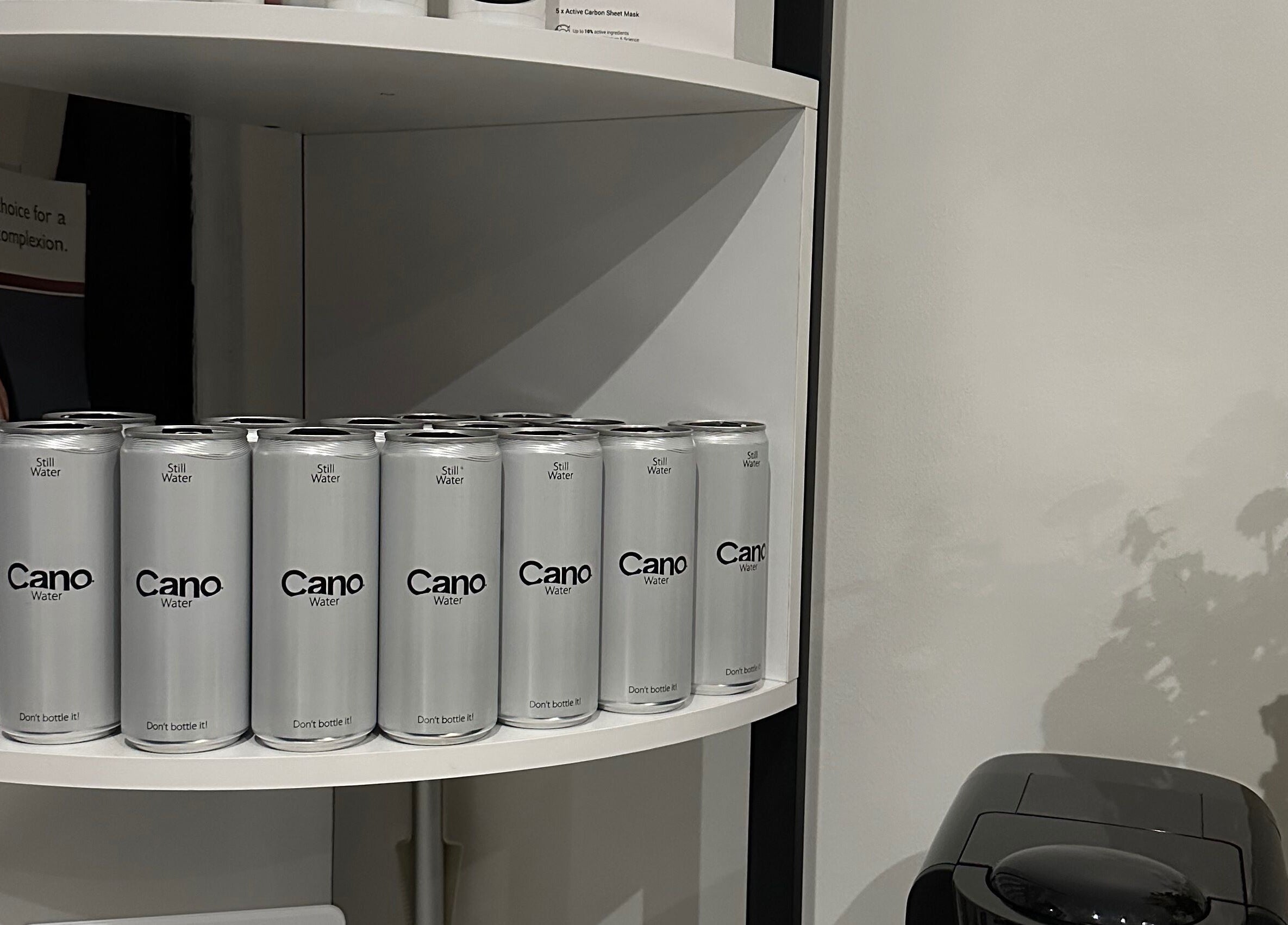 Array of Cano Water cans on display at Lash Me, Hounslow, England, GB, alongside flowers and a coffee machine.