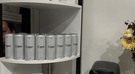 Array of Cano Water cans on display at Lash Me, Hounslow, England, GB, alongside flowers and a coffee machine.