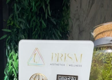 Decorative display at Prism Aesthetics & Wellness, London, England, GB, featuring lush greenery and a logo.