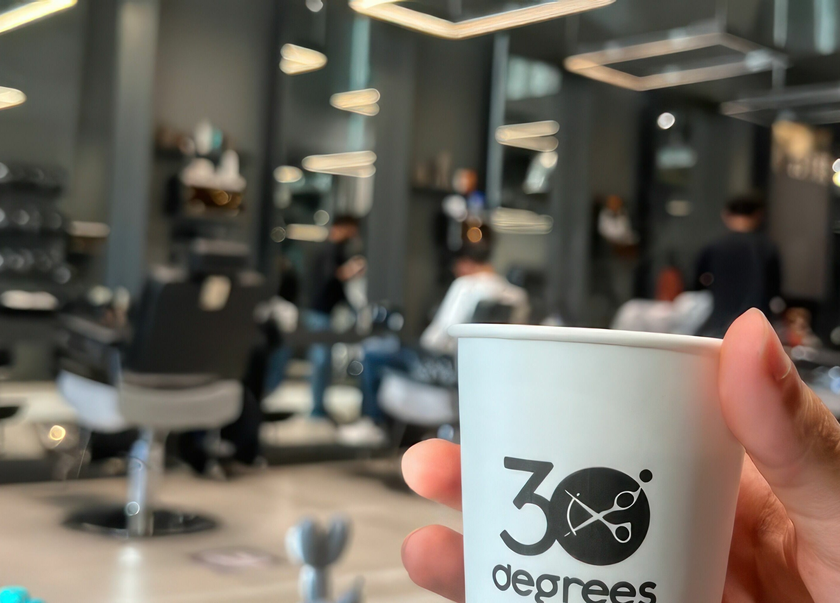 Inside AlNarjis 30 Degrees Barbershop in Riyadh, showcasing a cozy seating area and branded coffee cup.