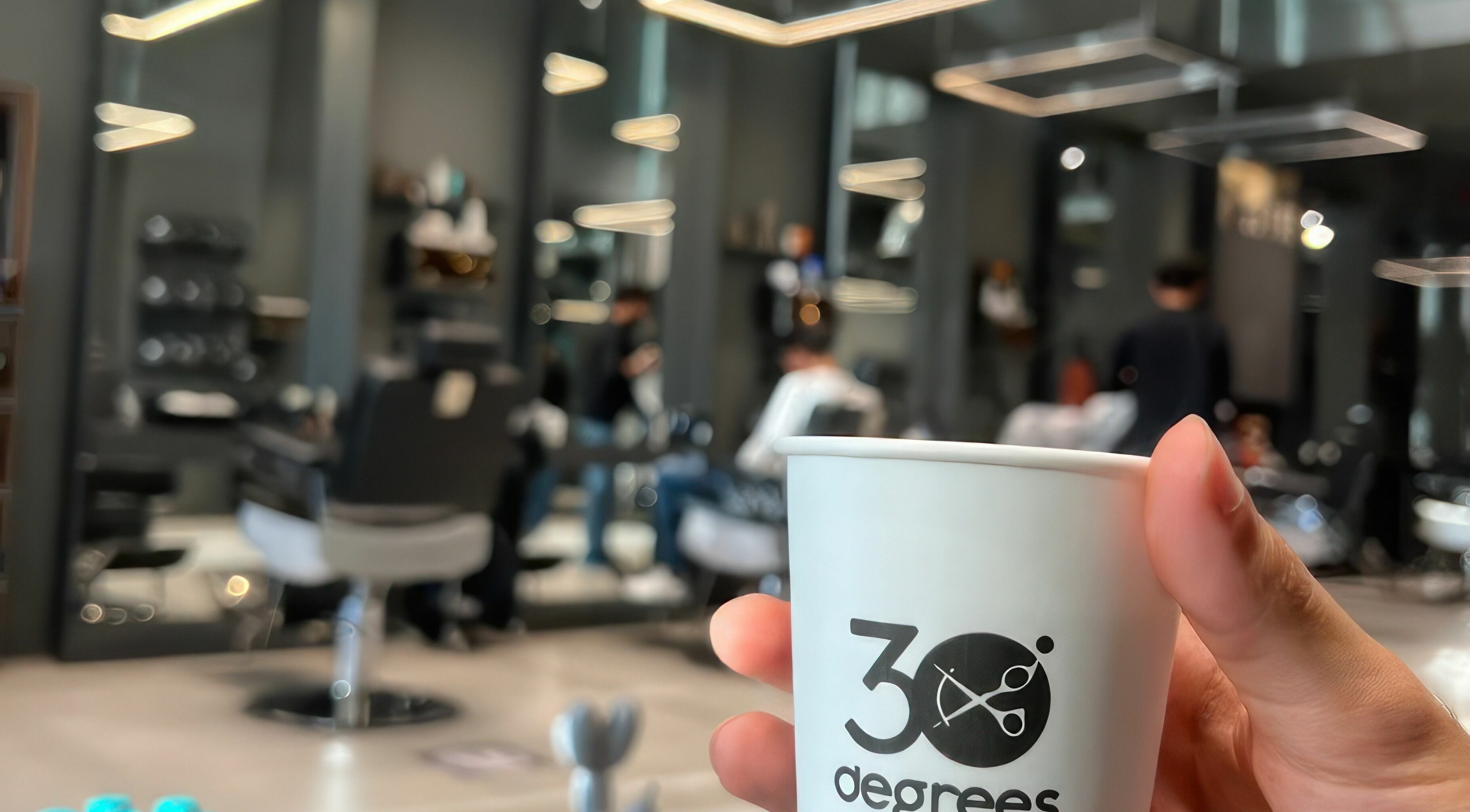 Inside AlNarjis 30 Degrees Barbershop in Riyadh, showcasing a cozy seating area and branded coffee cup.