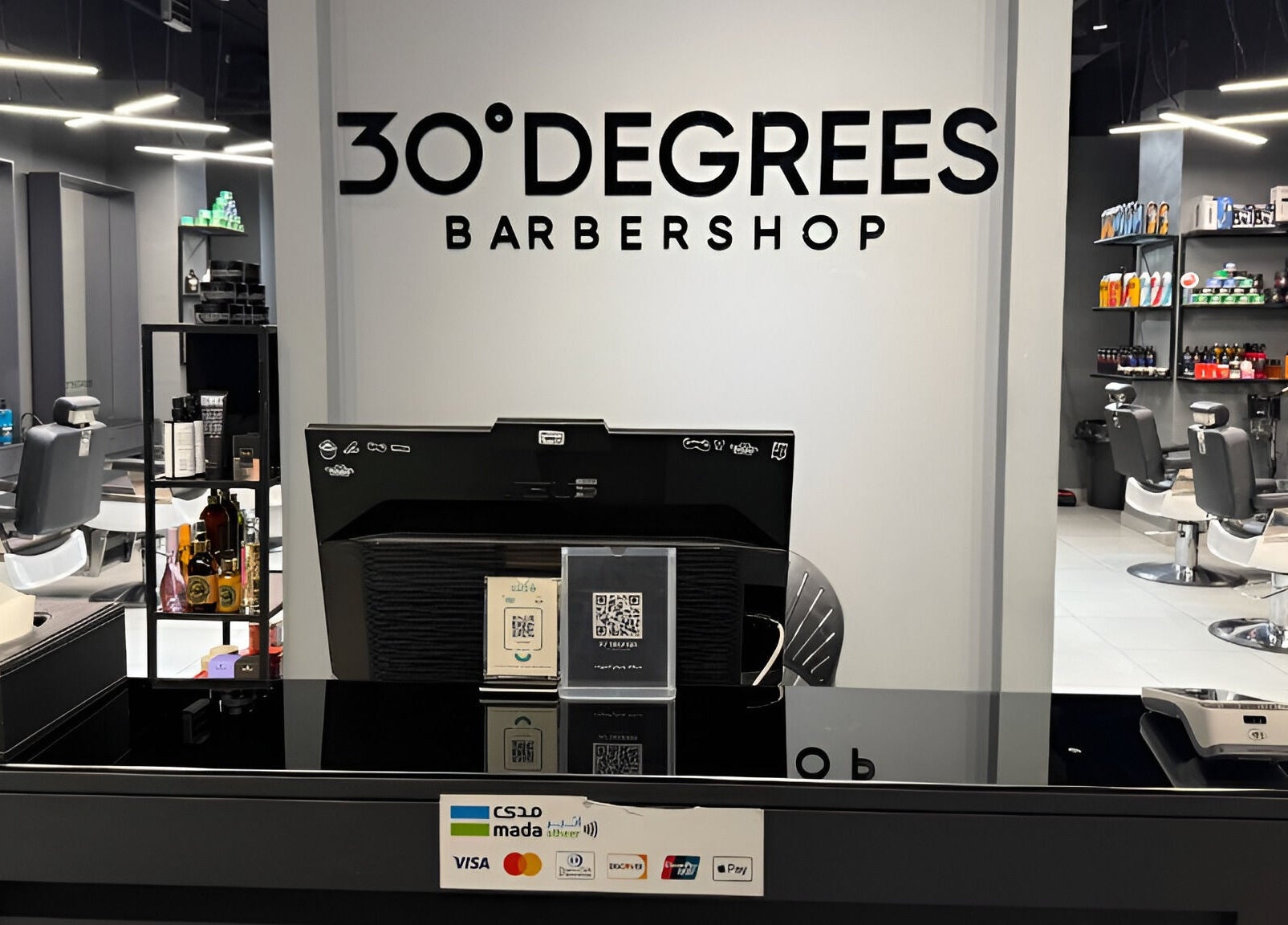Reception desk at Jeddah 30 Degrees Alnaeem barbershop, Jeddah, Makkah Province, SA, with sleek chairs and products.