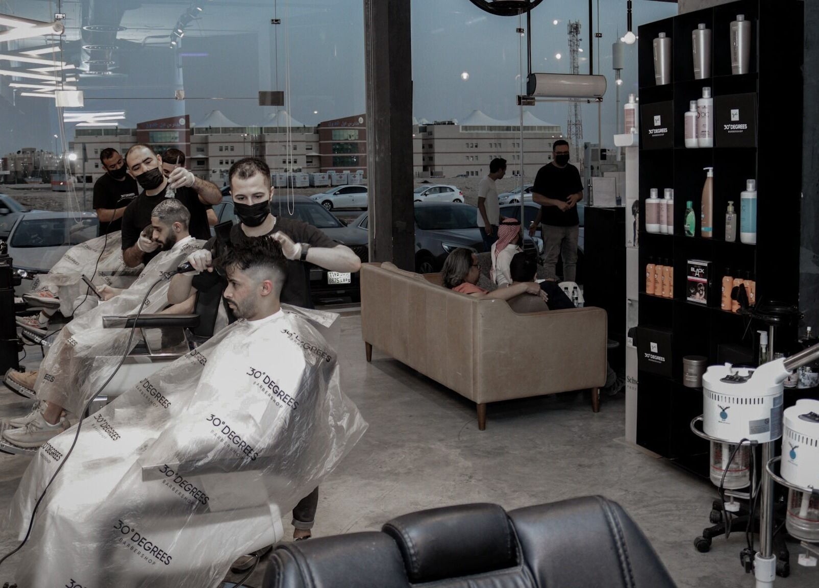 Modern interior of AlYasmin 30 Degrees, Riyadh, SA, showcasing stylish barbers at work and product display.