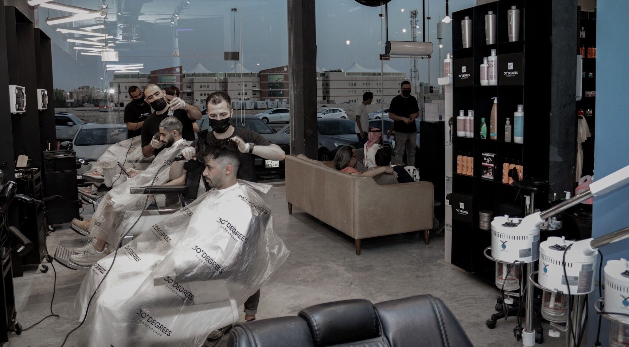 Modern interior of AlYasmin 30 Degrees, Riyadh, SA, showcasing stylish barbers at work and product display.
