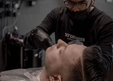 Professional barber at ✂️ خدمه الحلاقة المنزلية – Home Services in Riyadh trimming client's beard.